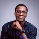 Charming young man in eyeglasses posing confidently with a smile against a purple background.