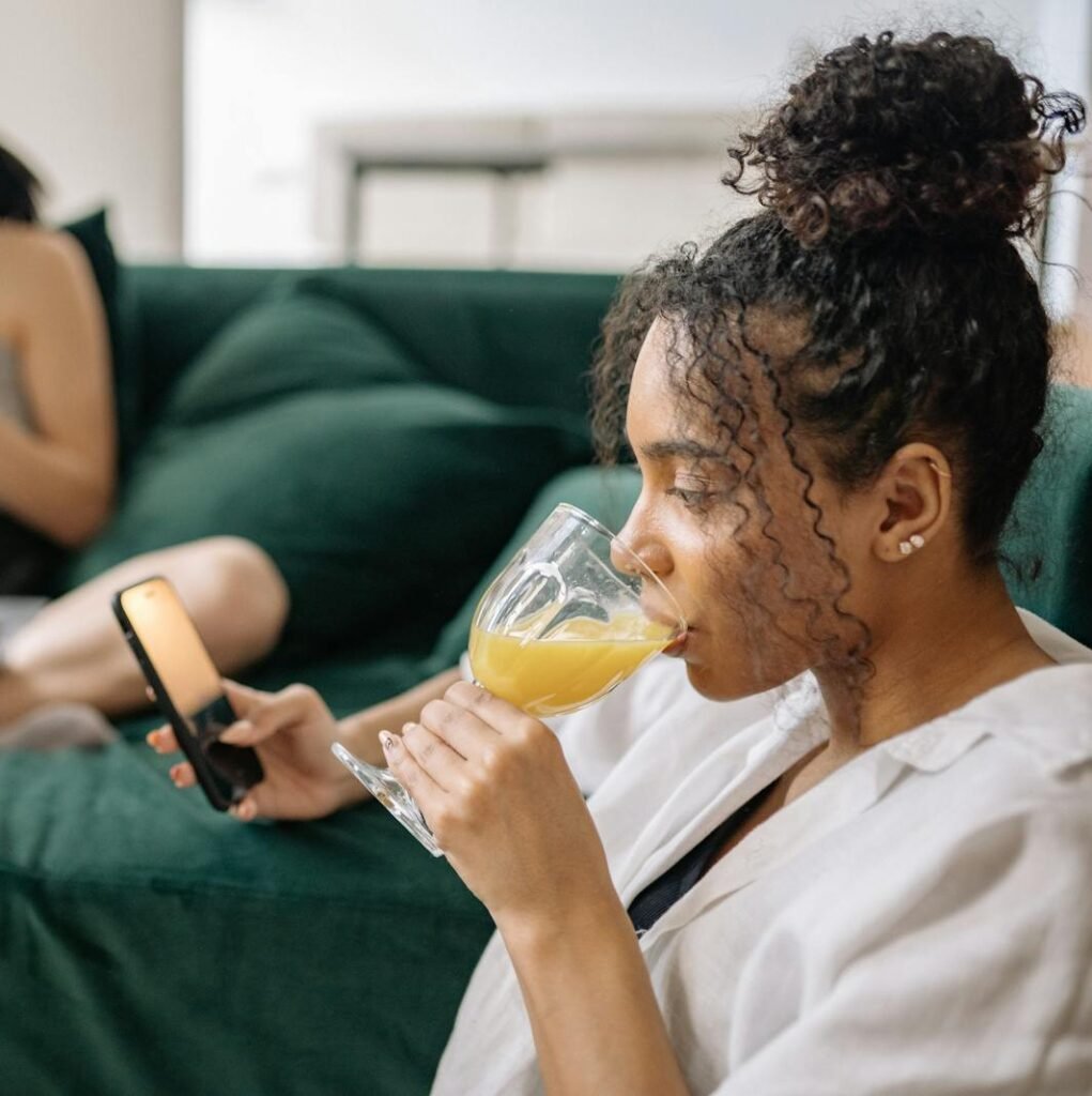 Two young women enjoying drinks at home, one with a phone and another with a laptop.